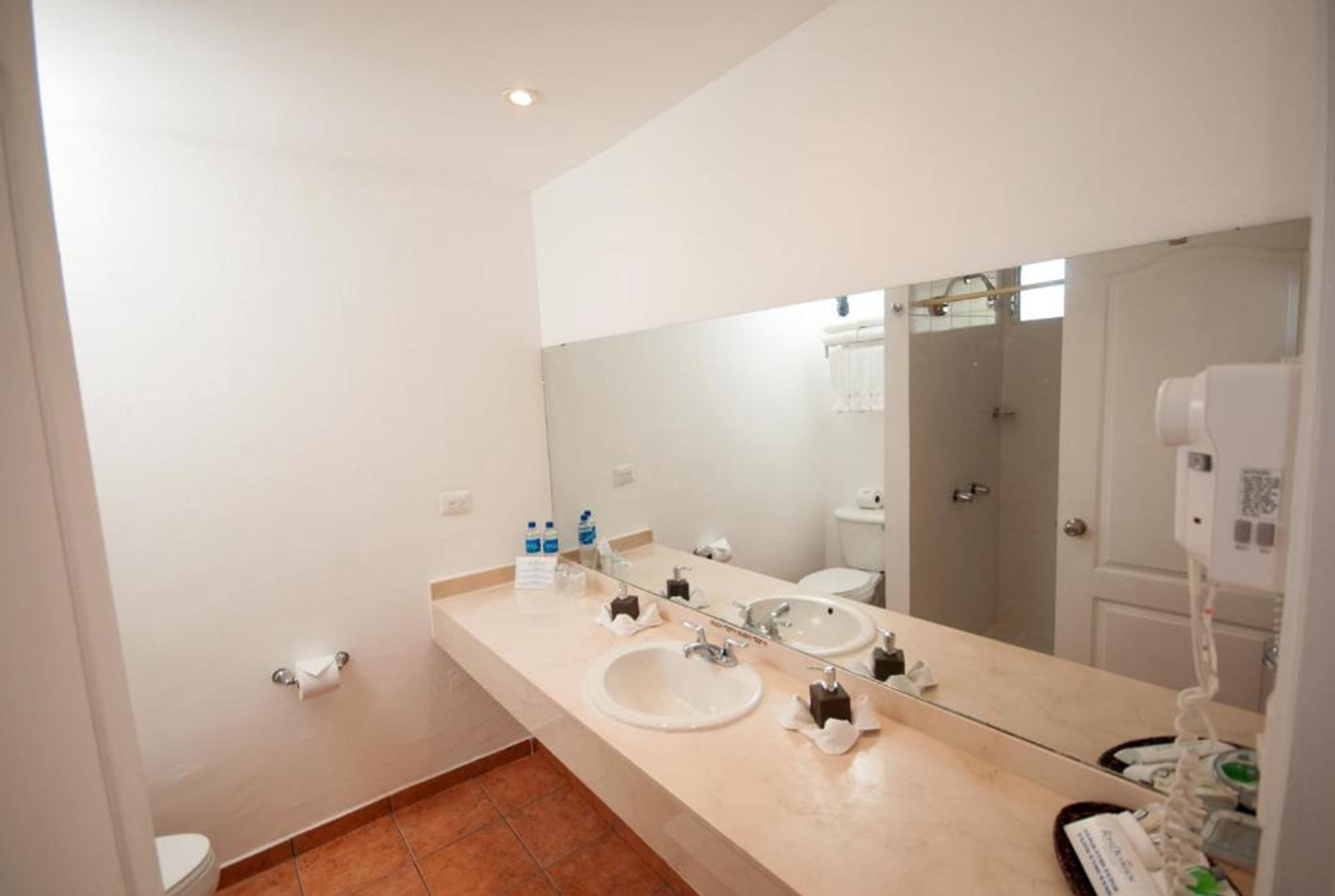 A modern bathroom with a large mirror, two sinks, a toilet, and a hairdryer.