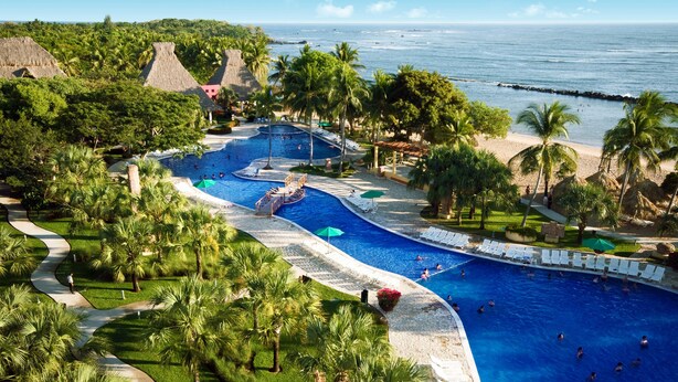 Un resort con una gran piscina, palmeras y vistas a la playa.
