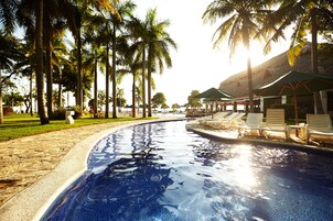 Piscina com espreguiçadeiras e guarda-sóis, rodeada por palmeiras.