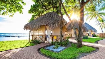 A beachfront resort with thatched-roof huts, a paved walkway, and a view of the ocean.