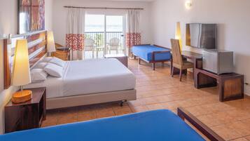 A hotel room with a bed, a desk with a television, a chair, and a view of the ocean through the balcony doors.