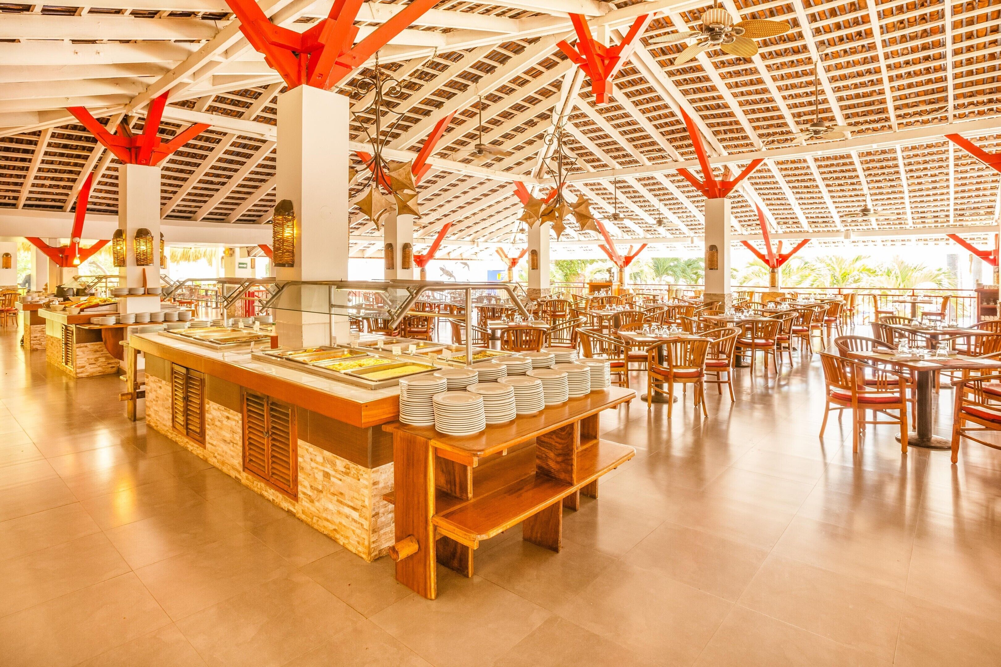 Un vaste espace intérieur aménagé en salle à manger, avec de nombreuses tables et chaises, un buffet proposant une variété de plats, et un plafond haut doté d’un design architectural remarquable.