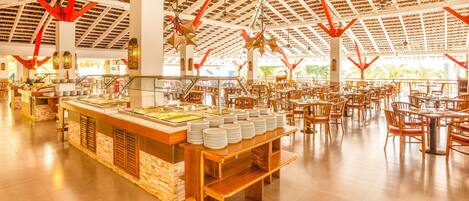 Un vaste espace intérieur aménagé en salle à manger, avec de nombreuses tables et chaises, un buffet proposant une variété de plats, et un plafond haut doté d’un design architectural remarquable.