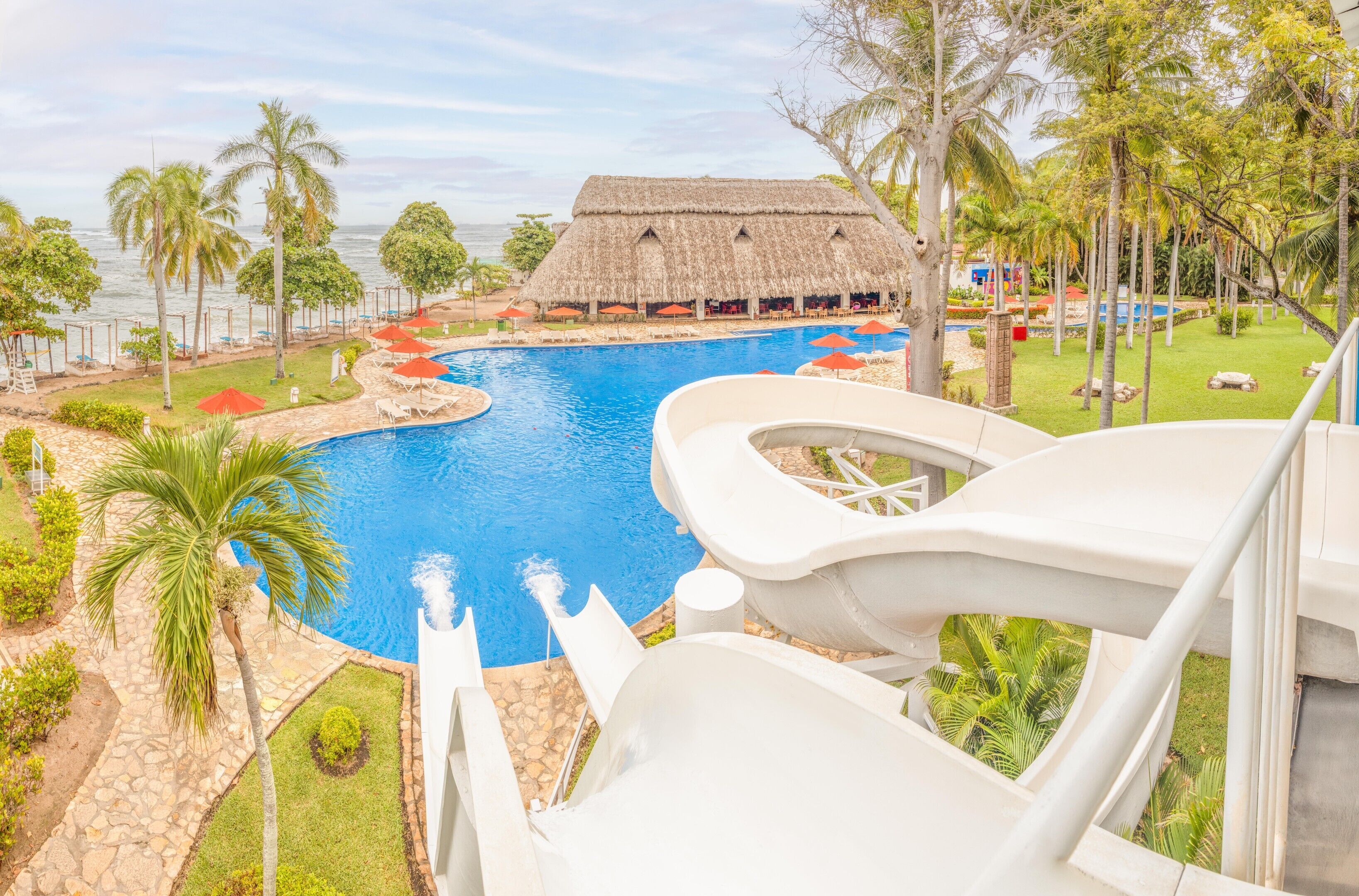A resort with a large pool, a thatched-roof building, and palm trees.