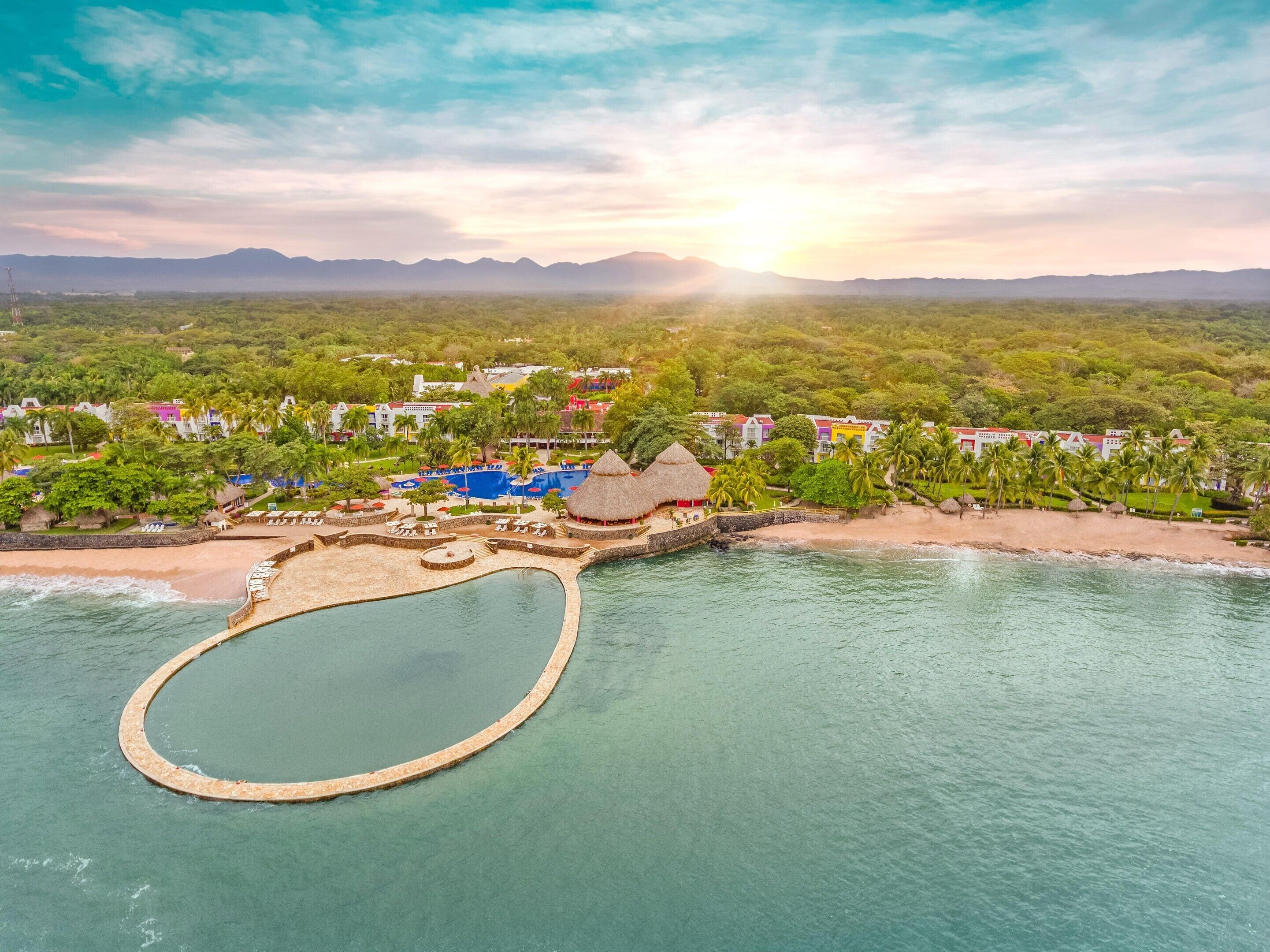 Un resort con una piscina grande, acceso a la playa y exuberante vegetación tropical.