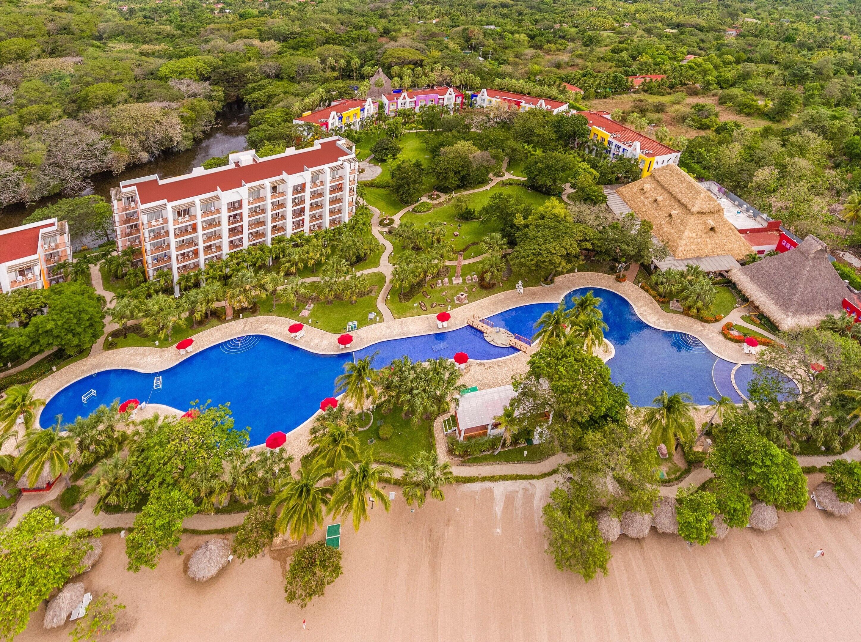 Ein Resort mit mehreren Schwimmbecken, einem großen Gebäude mit Balkonen und üppiger, umgebender Bepflanzung.