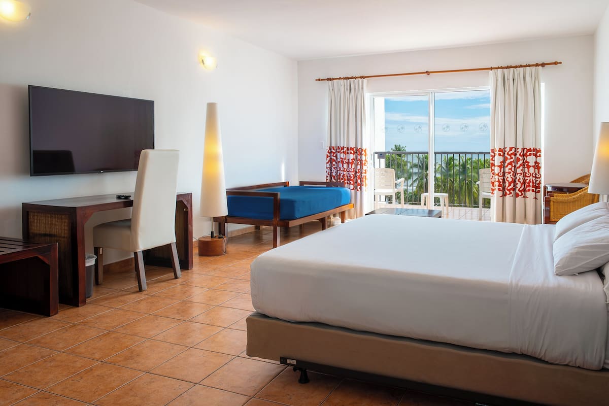 A hotel room with a bed, a desk, a chair, a TV, and a balcony with a view.