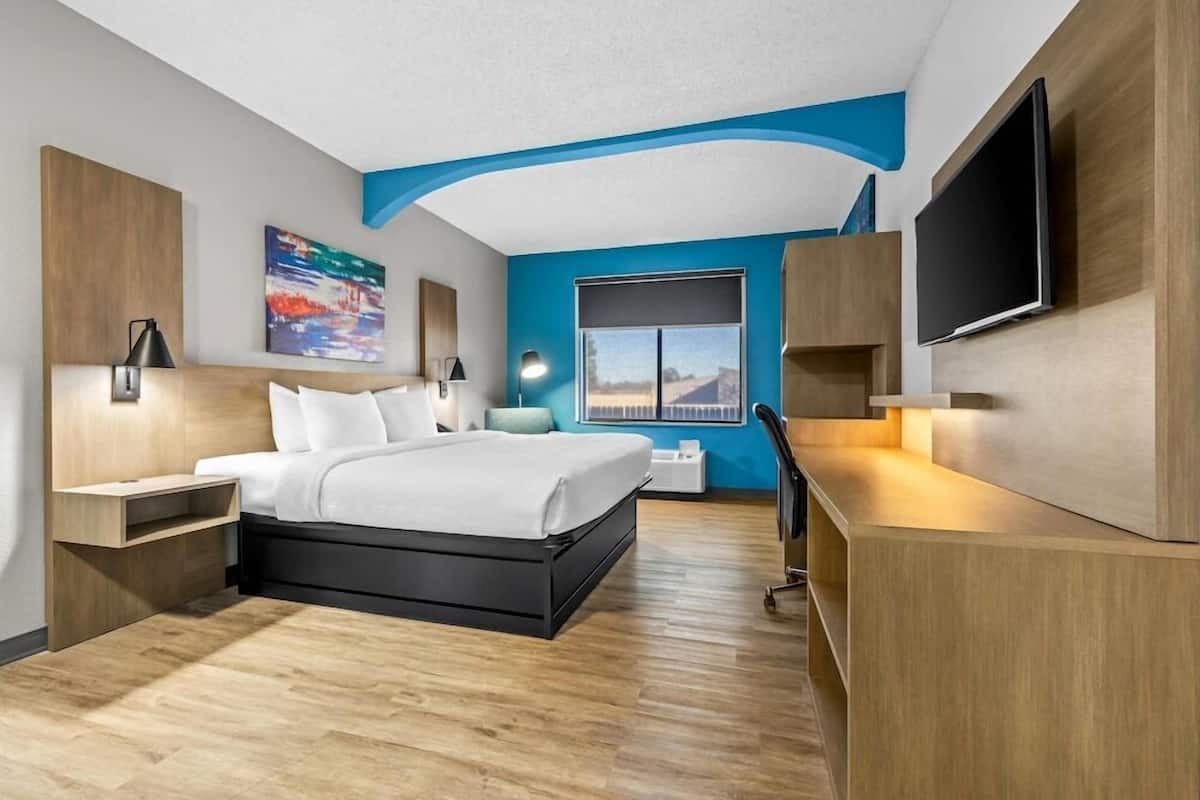 A modern hotel room with a bed, desk, TV, and artwork on the walls.