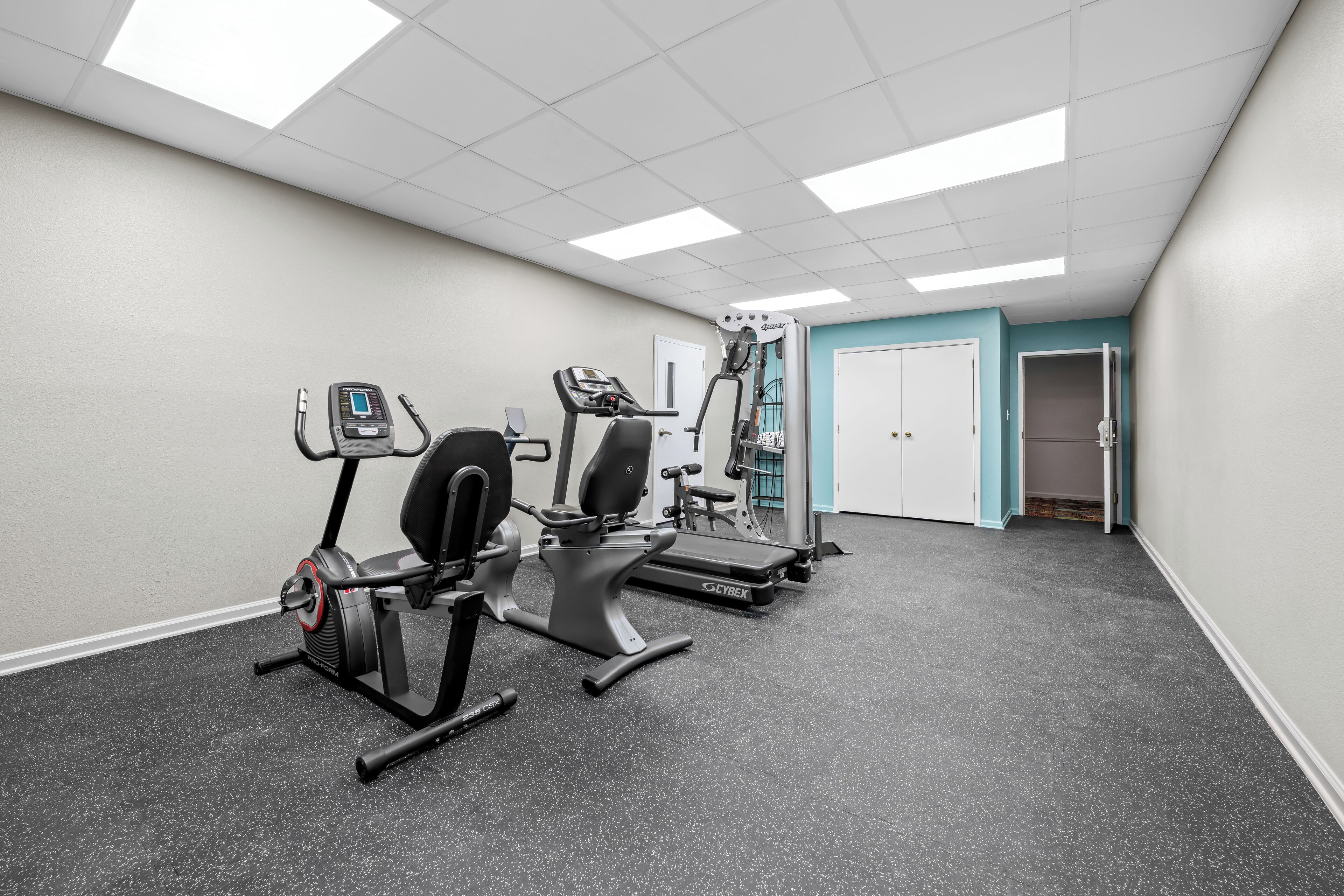A gym with cardio machines, a weight bench, and a door leading to another room.