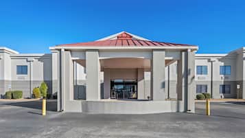 A modern building with a central entrance pavilion, large windows, and a parking area.