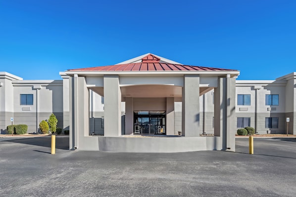 A modern building with a central entrance pavilion, large windows, and a parking area.