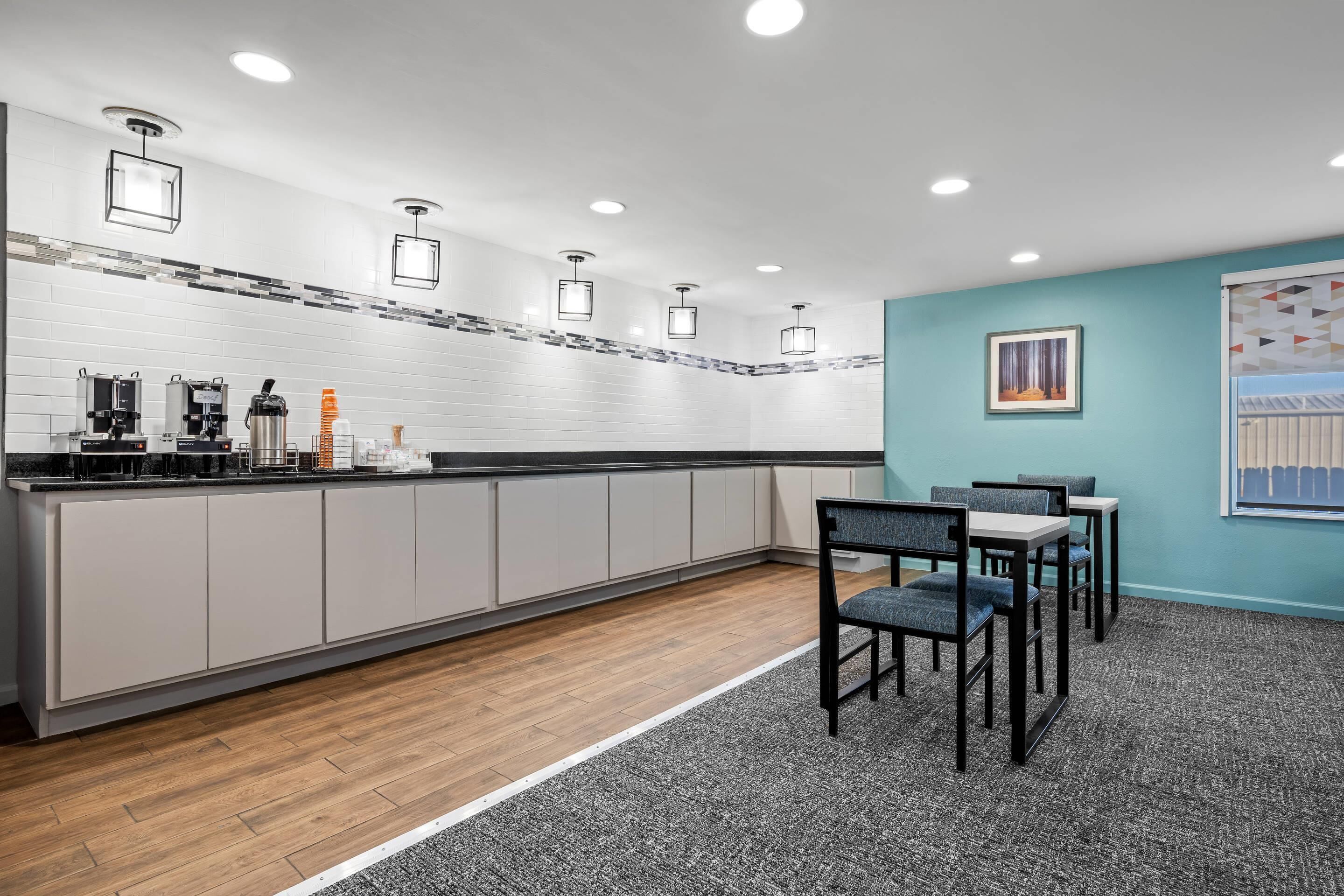A modern kitchen with white cabinets, a wooden countertop, and a dining area with chairs and a table.