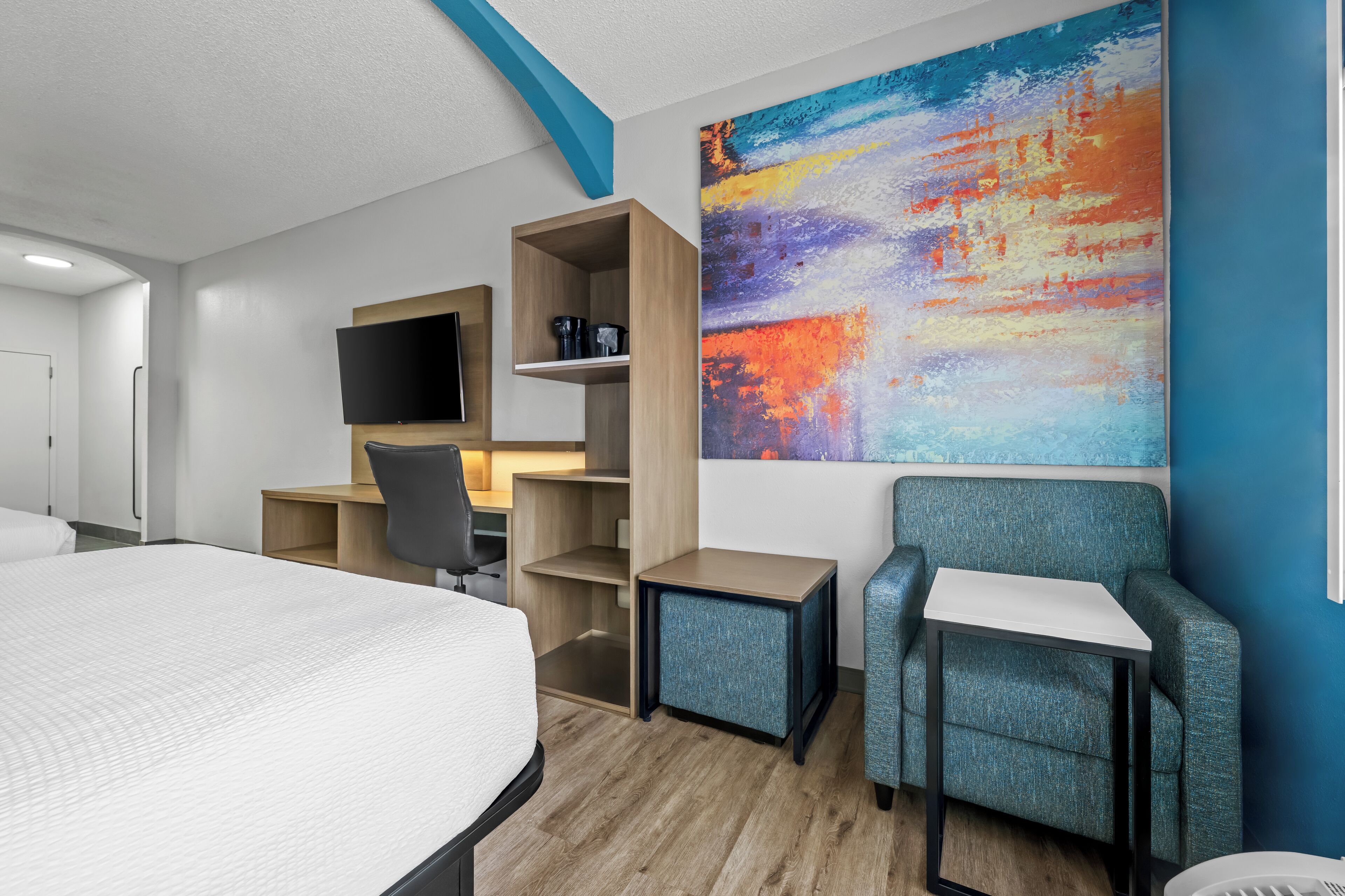 Una habitación de hotel con una cama, un escritorio, una silla, un televisor y un cuadro abstracto colorido en la pared.