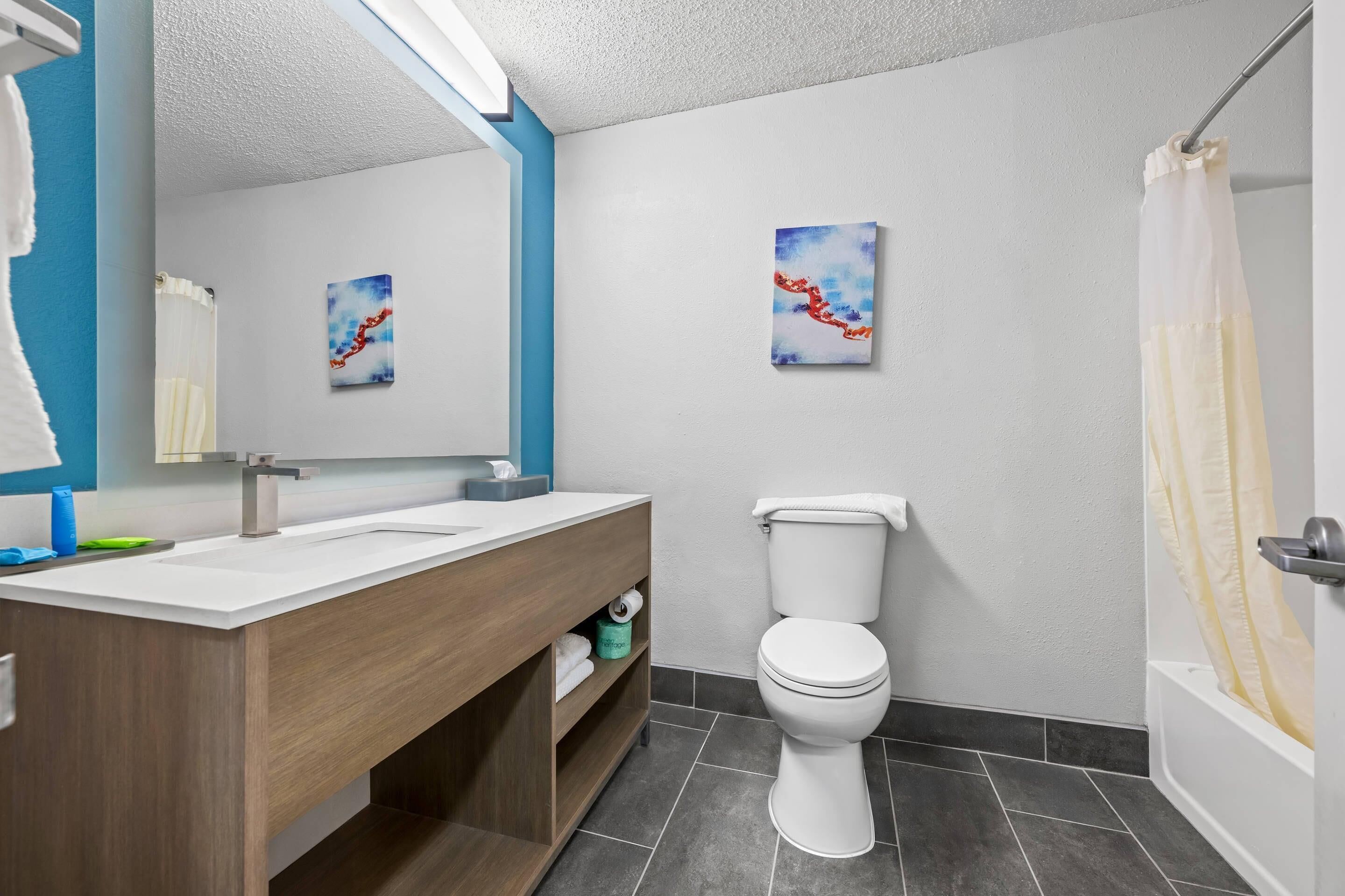 A modern bathroom with a wooden vanity, two sinks, a toilet, and a bathtub.