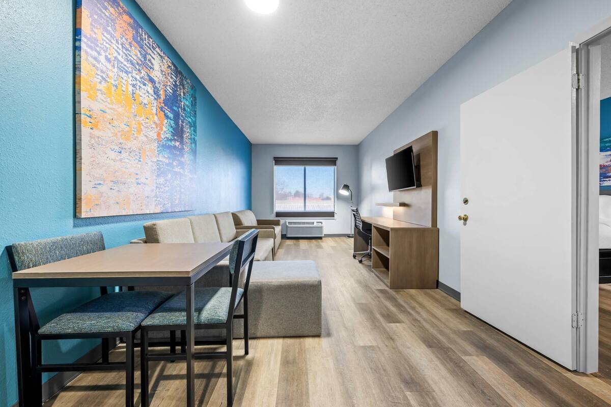 A modern room with a dining area, a large abstract painting, a TV, and a window with a view.