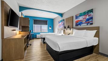 A modern hotel room with a large bed, a desk with a flat-screen TV, a chair, and a window.