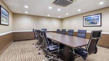 A conference room with a large table, six chairs, and two framed pictures on the walls.