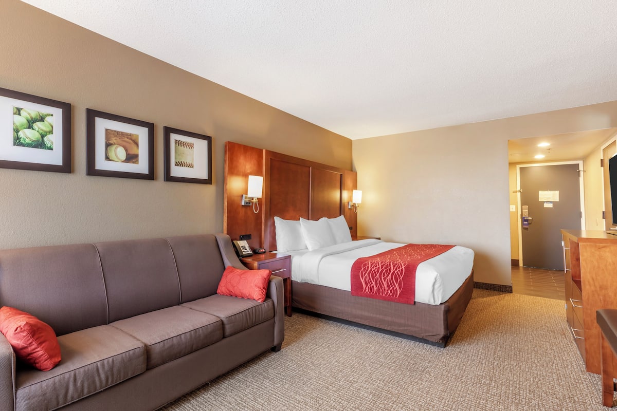 A hotel room with a bed, a sofa, a desk, and framed pictures on the wall.