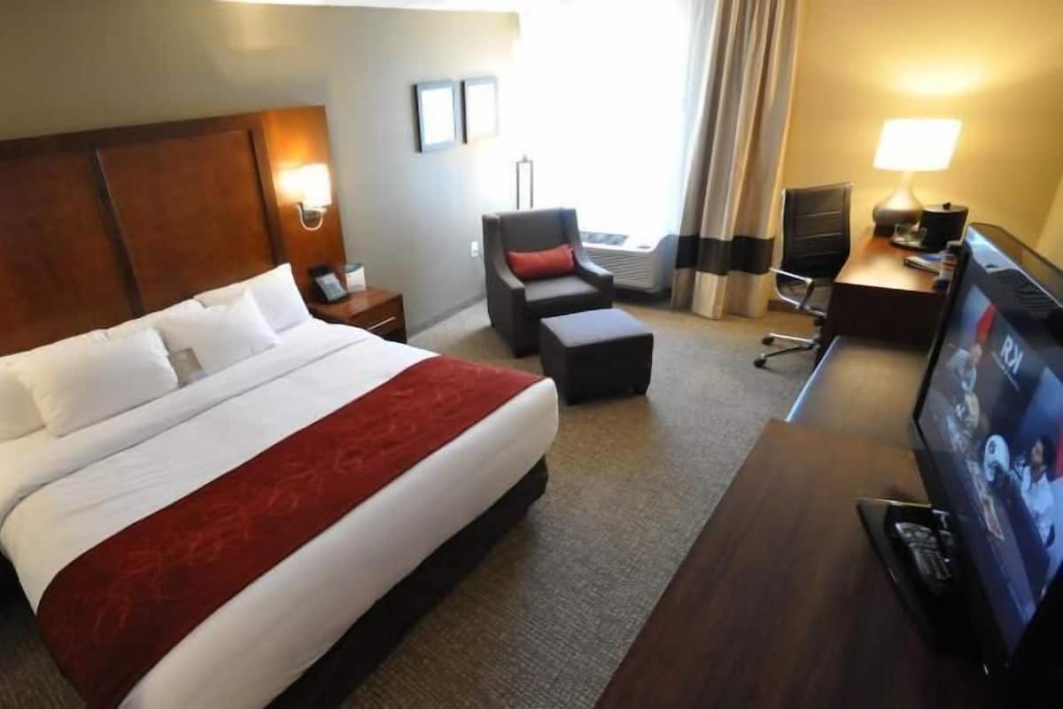 A hotel room with a large bed, a desk with a TV, a chair, and a desk lamp.