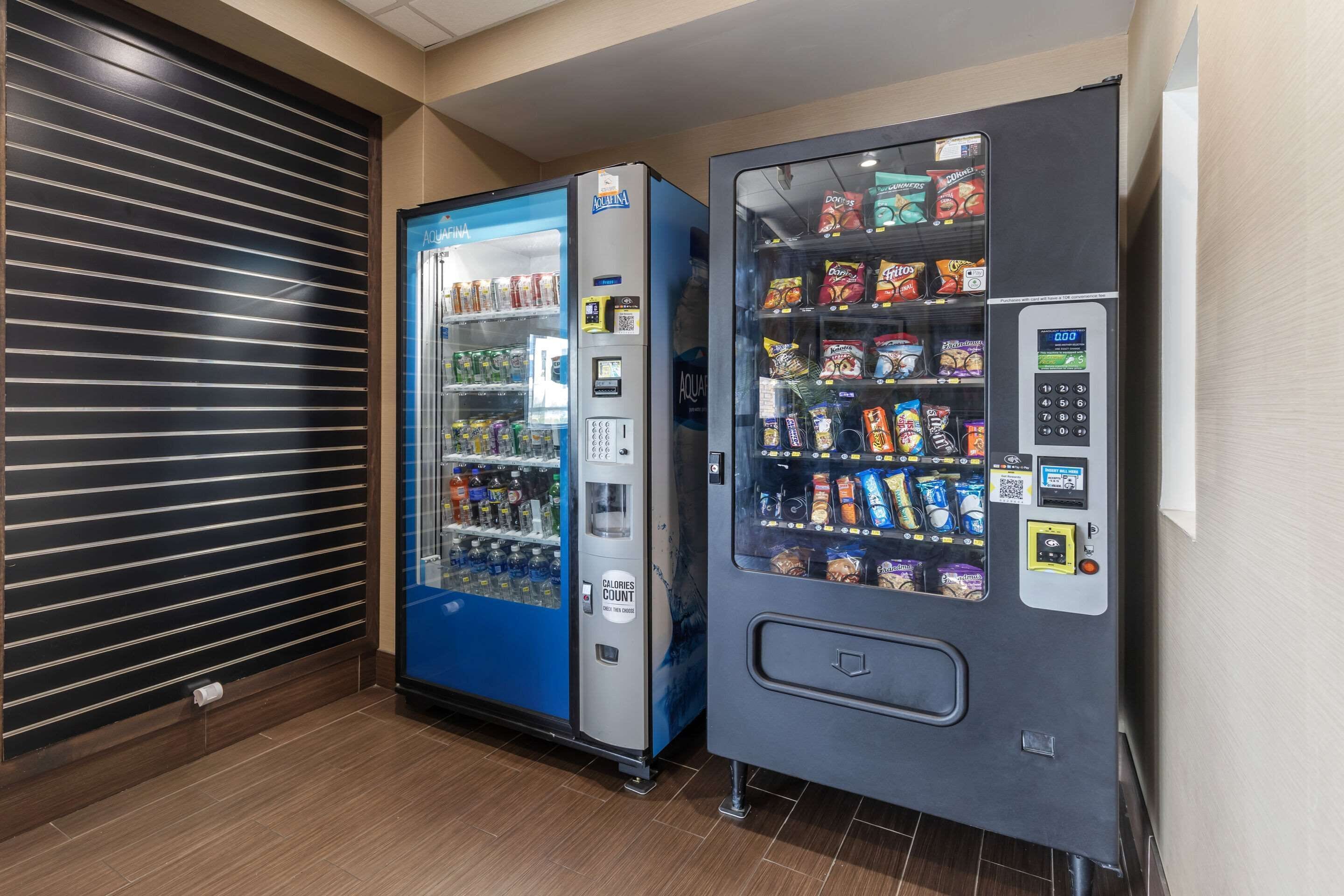Ein Automatenbereich mit einer blauen und einer grauen Maschine, beide gefüllt mit Snacks und Getränken.