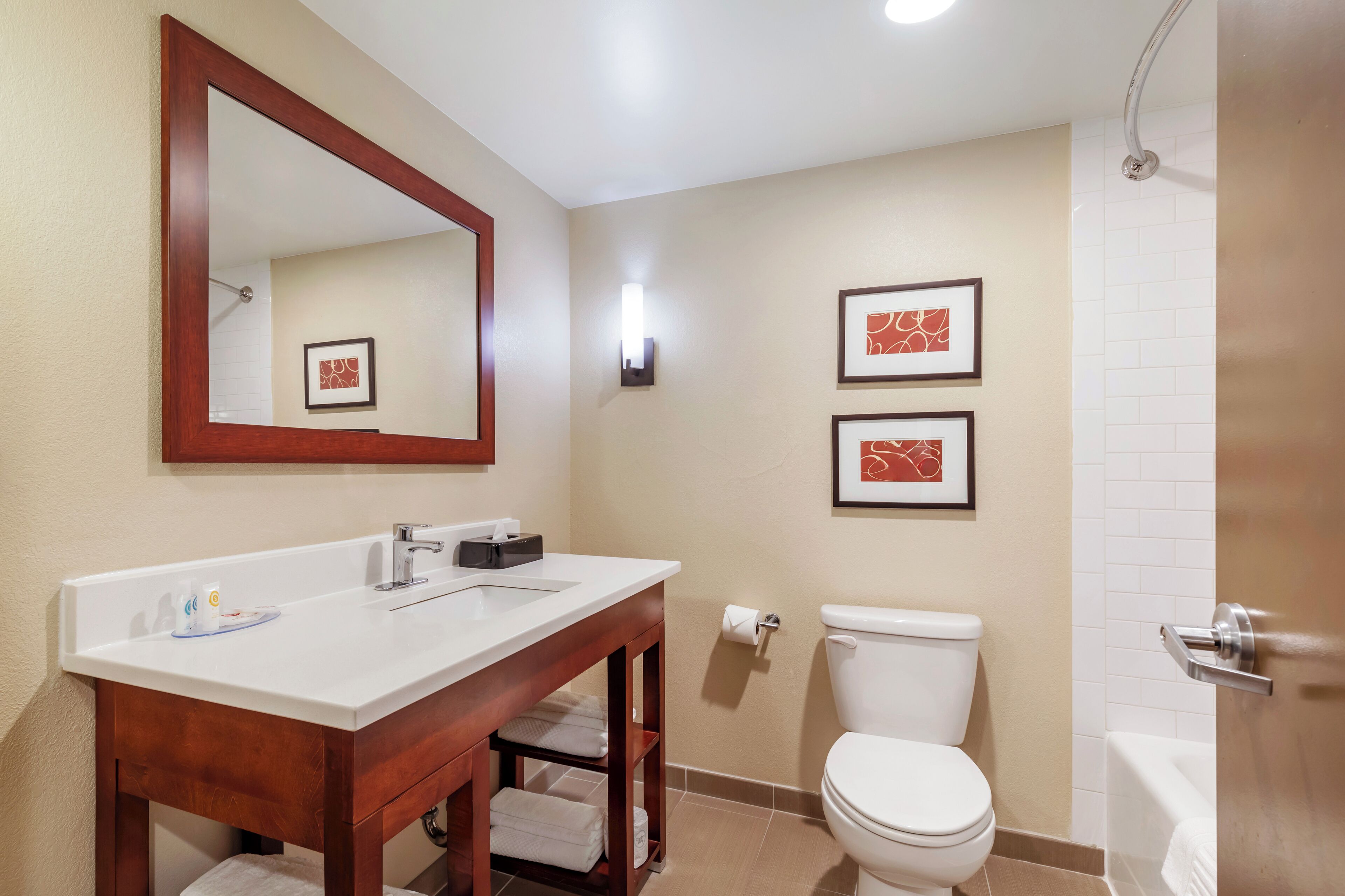 A bathroom with a white sink, wooden vanity, two framed pictures, a toilet, and a bathtub.