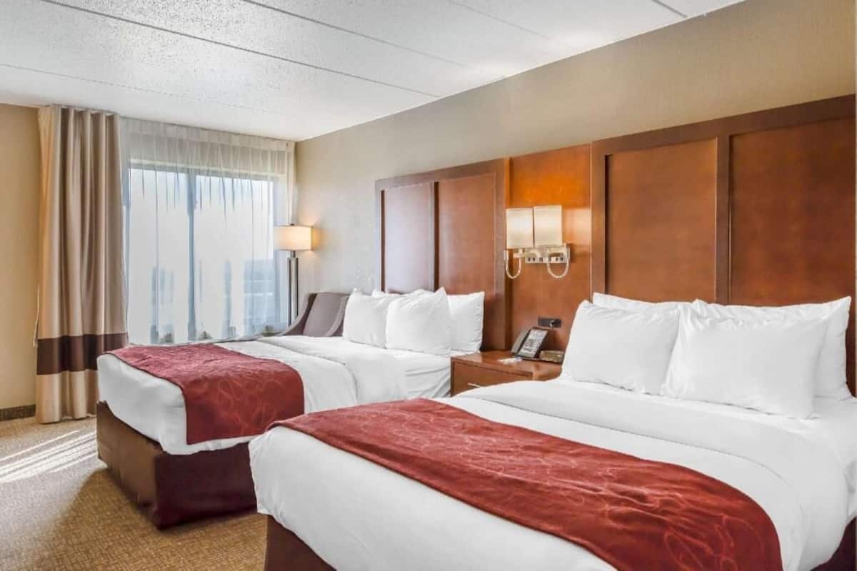 A hotel room with two beds, a desk, a lamp, and a view of the city.