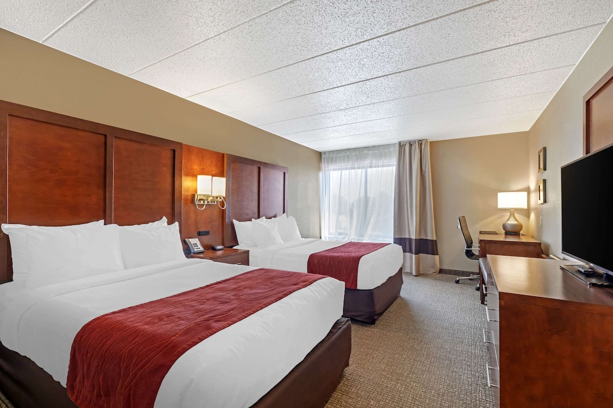 A hotel room with two beds, a desk, a television, and a window with curtains.