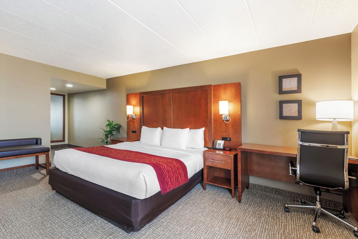 A hotel room with a large bed, bedside tables, a desk with a chair, and a lamp.