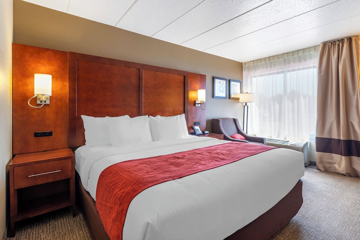 A hotel room with a large bed, wooden headboard, bedside lamps, a desk, and a chair.