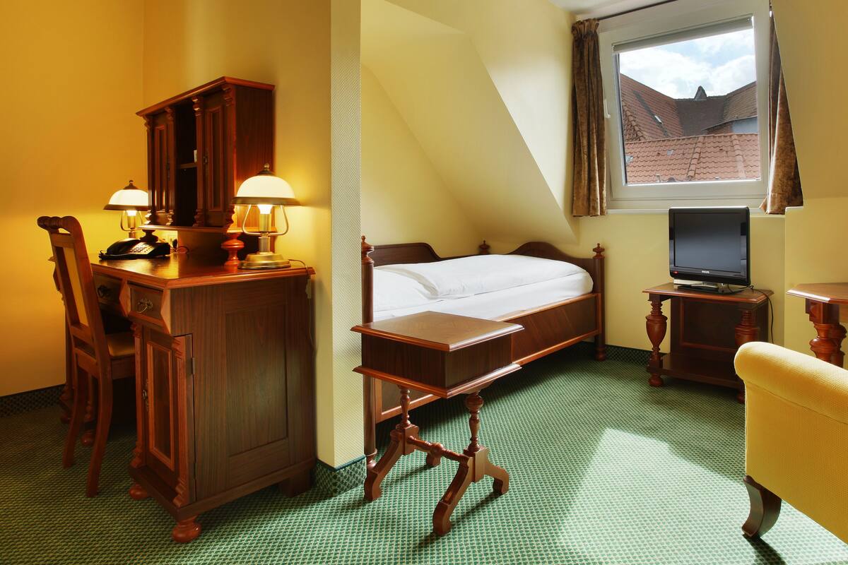 A hotel room with a bed, desk, chair, lamp, and a television.
