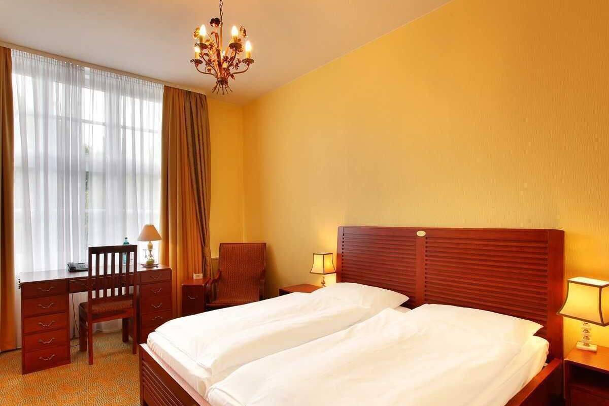 A hotel room with a double bed, a desk, a chair, and a chandelier.