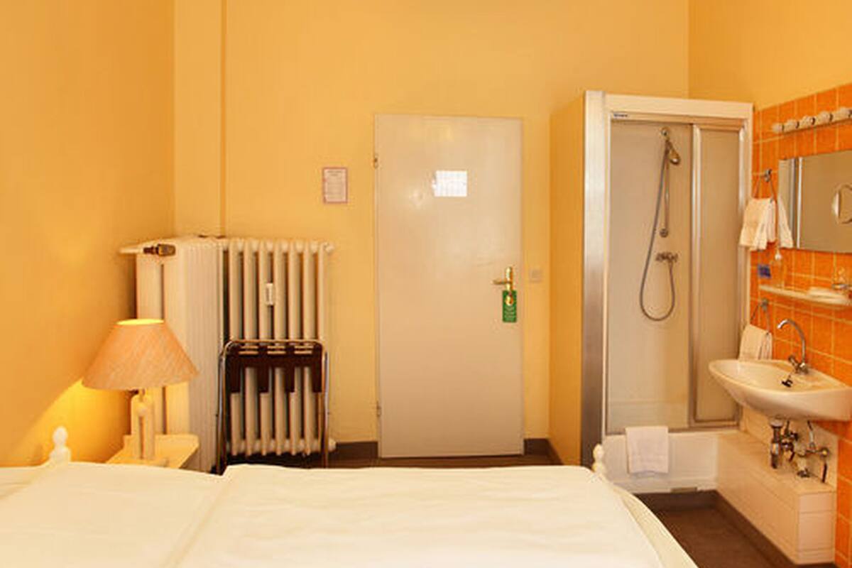A hotel room with a bed, a radiator, a door, a shower, and a sink.