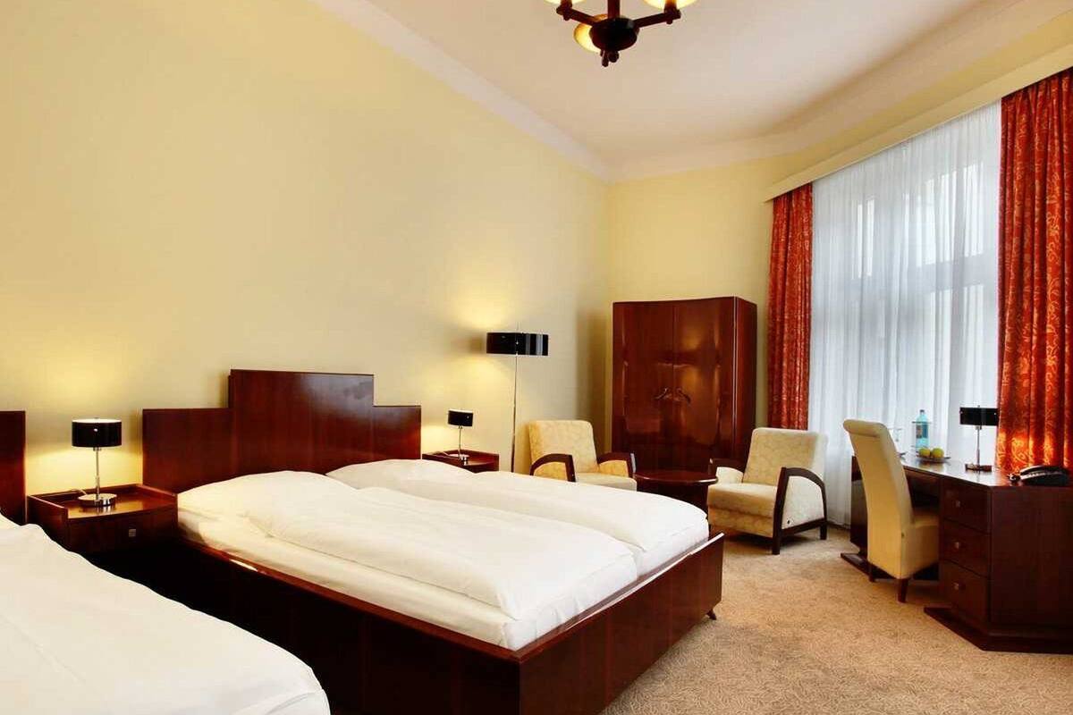 A hotel room with two beds, a desk, a chair, a wardrobe, and a large window with curtains.