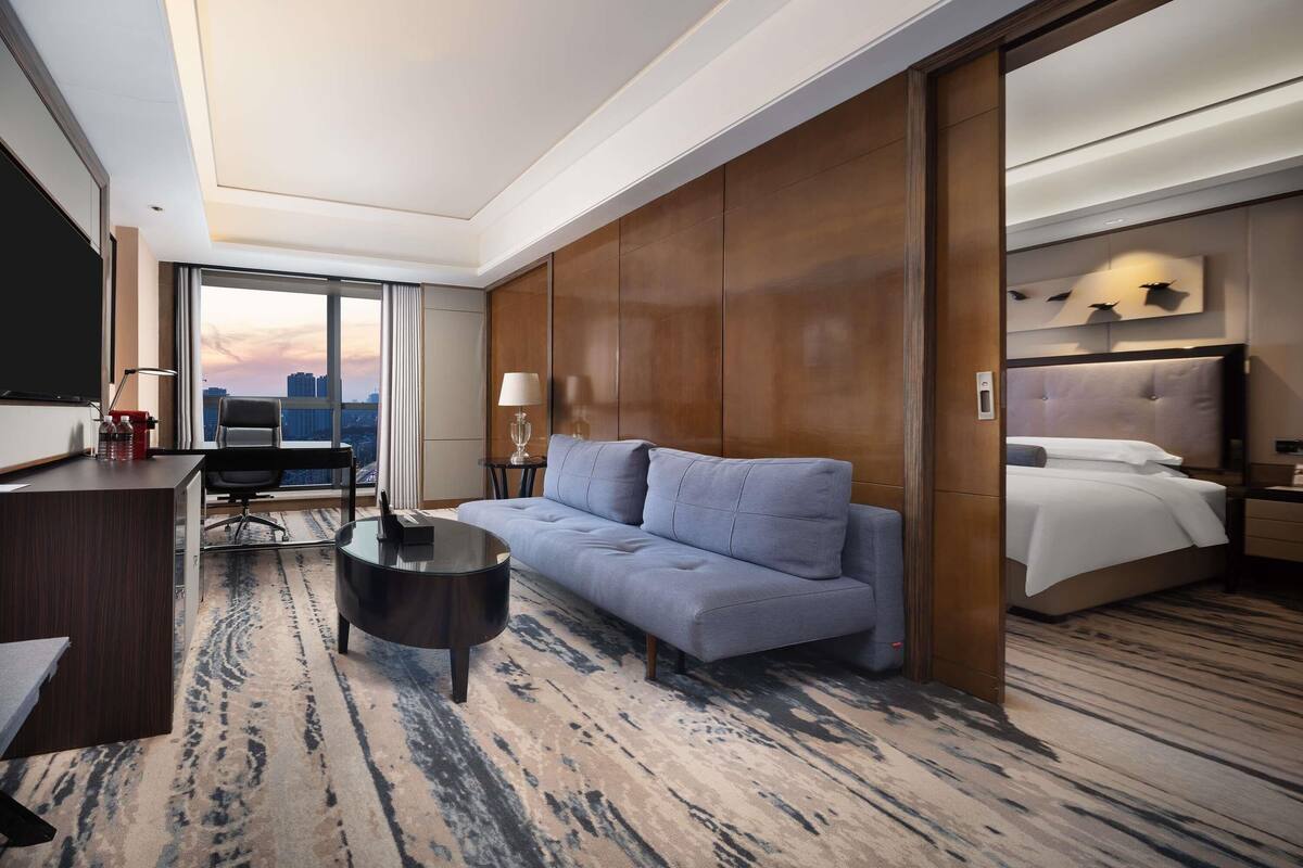 Habitación de hotel con una cama grande, un sofá, un escritorio y vistas a la ciudad.