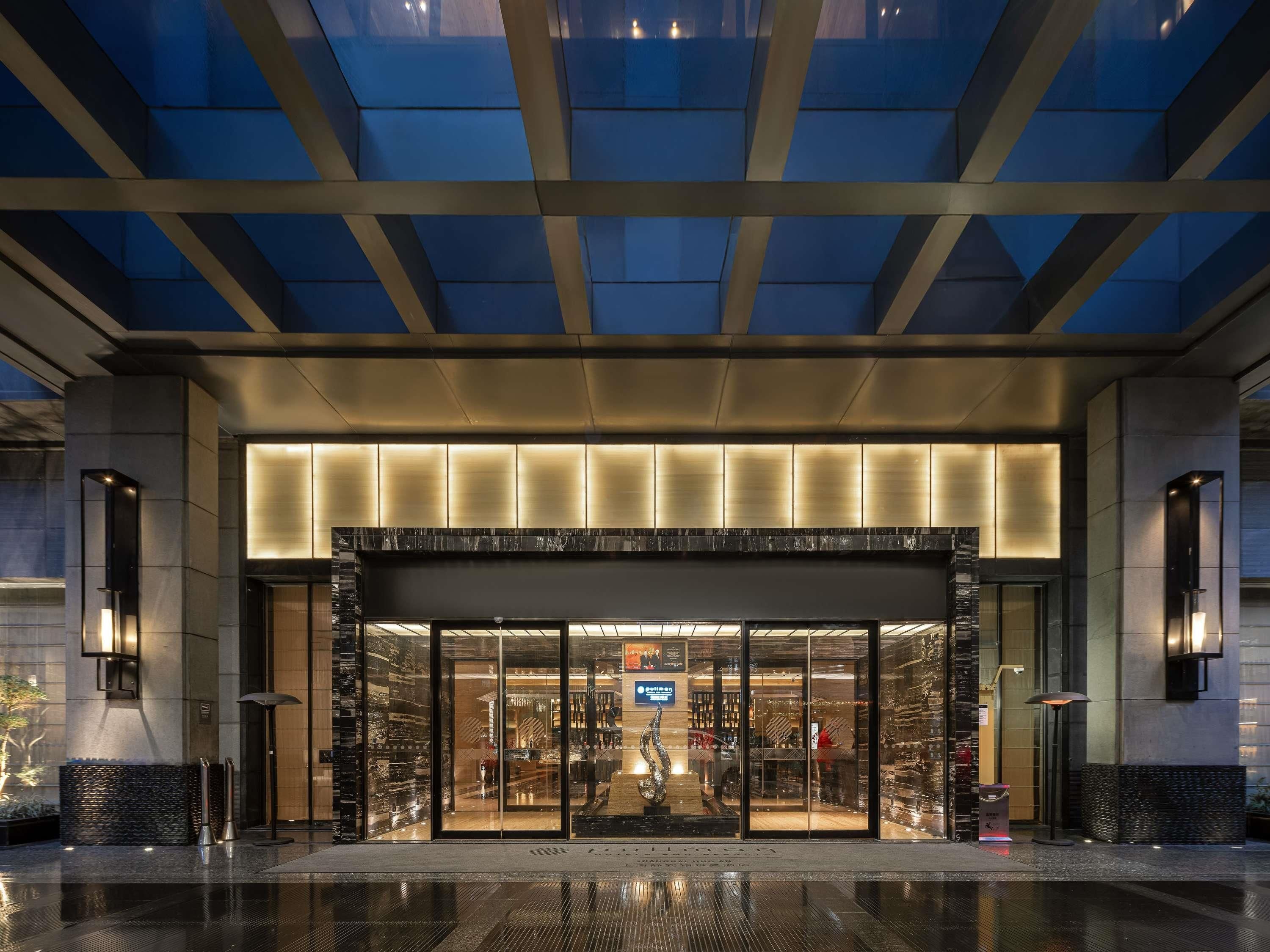 Una entrada de hotel moderna con fachada de vidrio, acceso central y techo con diseño geométrico.