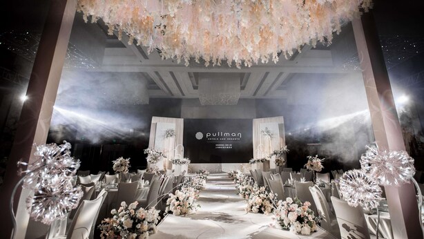 A banquet hall with a central stage, rows of tables with floral centerpieces, and a decorative chandelier. - Pullman Shanghai Jing An (Shanghai)