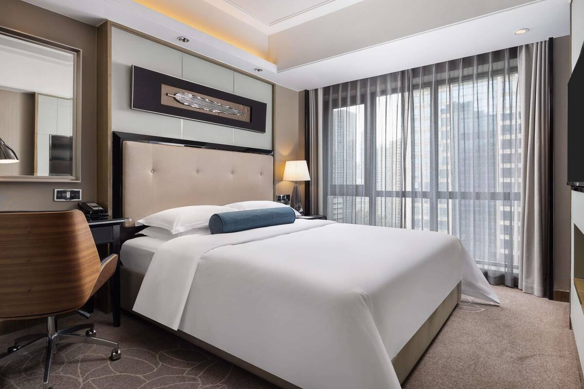 Una habitación de hotel con una cama grande, un escritorio, una silla, un espejo y una ventana con cortinas.