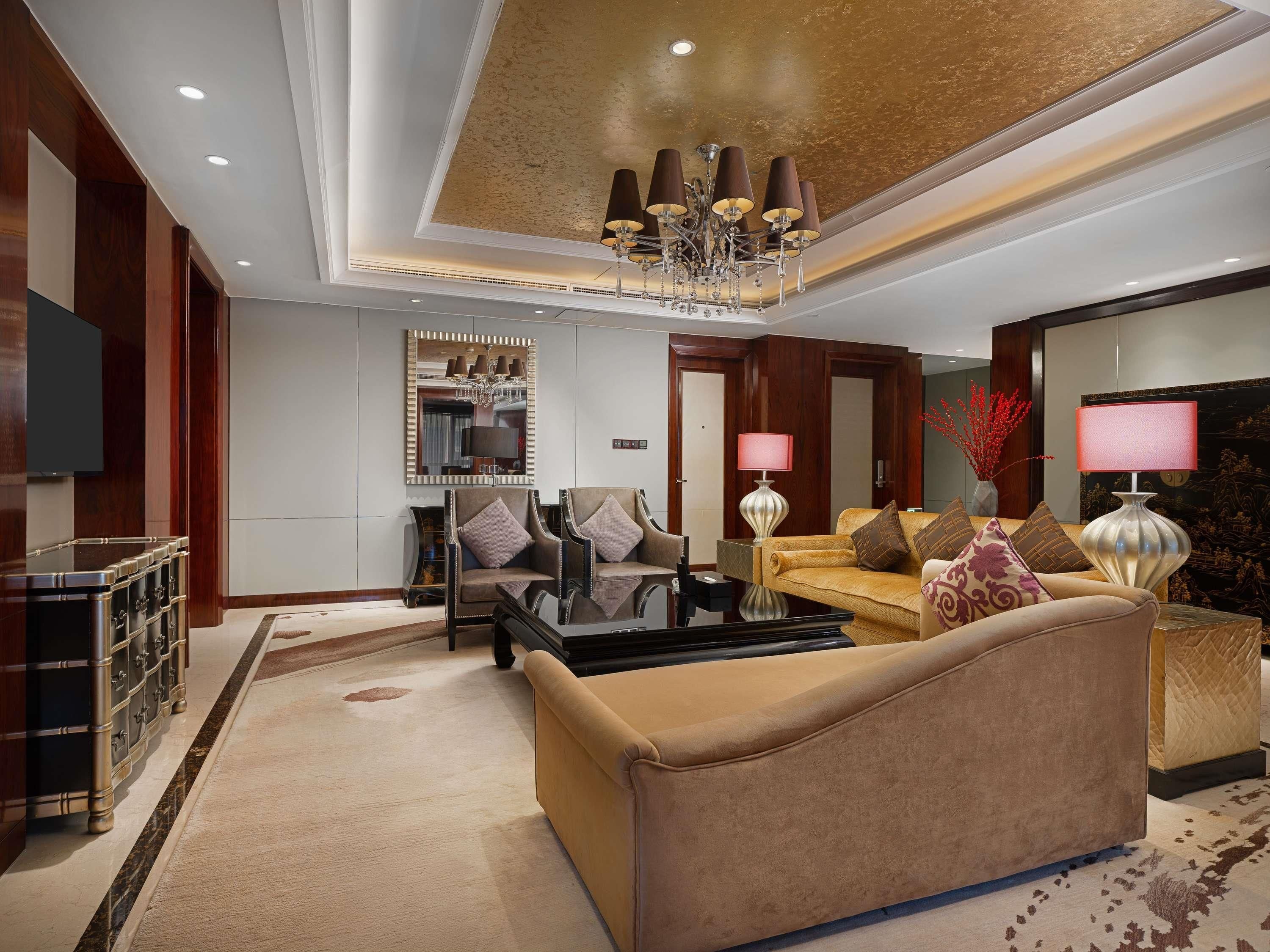 Una sala moderna con un sofá, sillones, una mesa de centro, televisor, candelabro y un espejo decorativo.