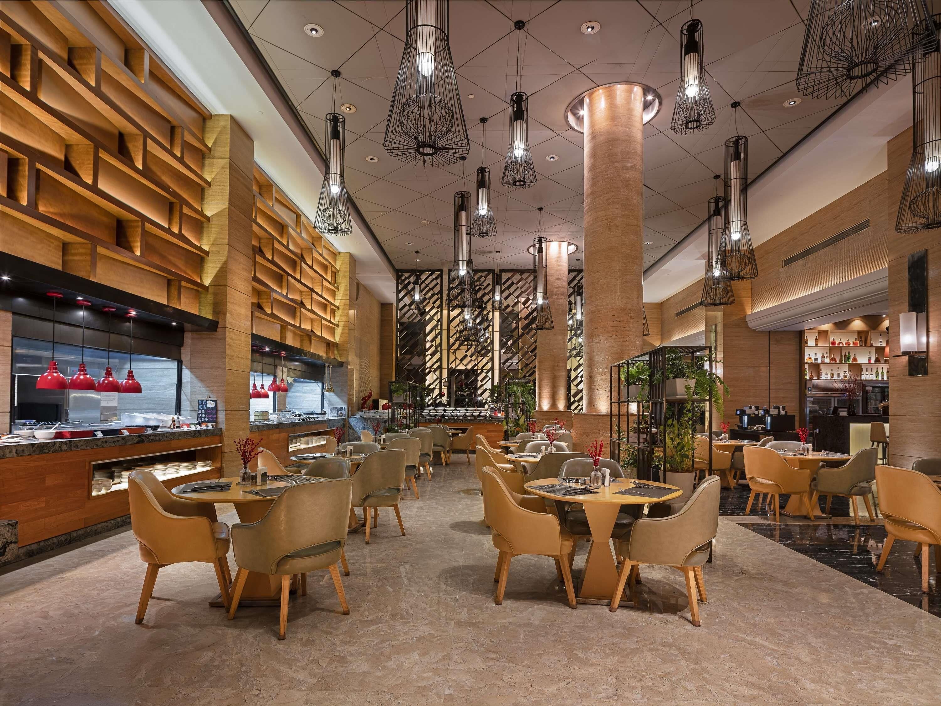 Un interior de restaurante moderno con varias mesas y sillas para comer, una zona de cocina y un diseño de pared con motivos.