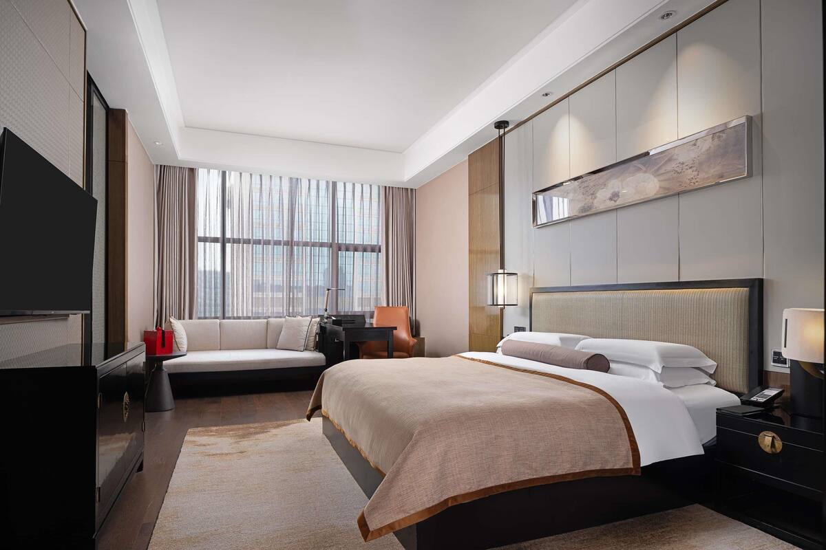 Una habitación de hotel moderna con una cama grande, televisión, escritorio y ventana con cortinas.