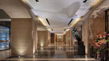 A modern hotel lobby with a marble floor, large columns, and a central staircase.