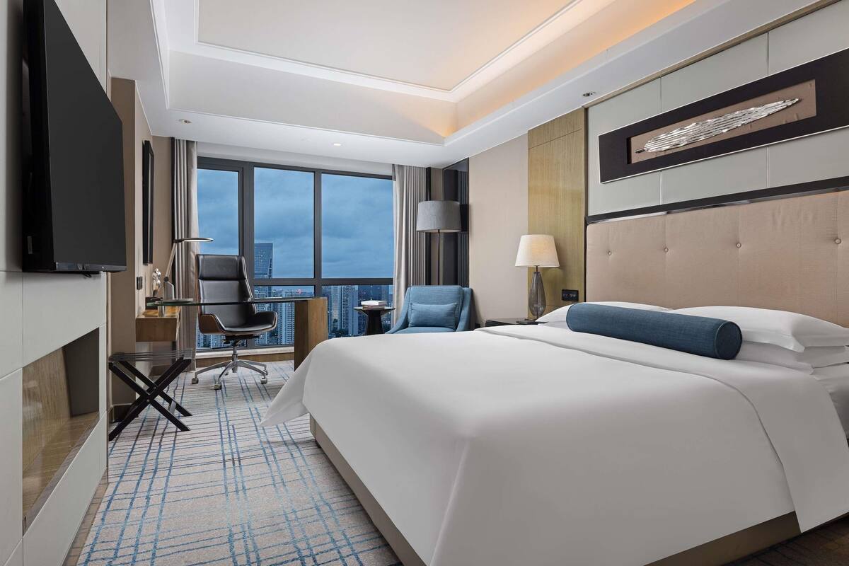 Una habitación de hotel moderna con una cama grande, televisión, escritorio y una silla.
