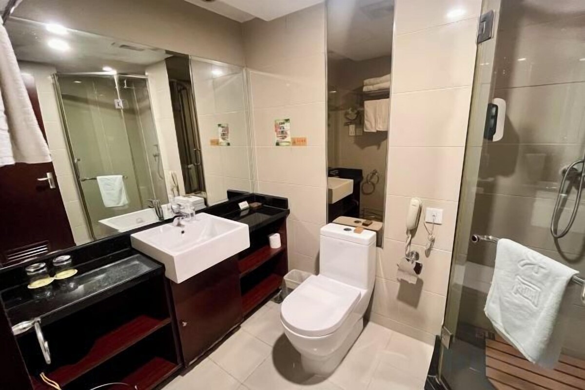 Une salle de bain avec une douche à parois de verre, des toilettes blanches, un lavabo avec un miroir et un porte-serviettes.