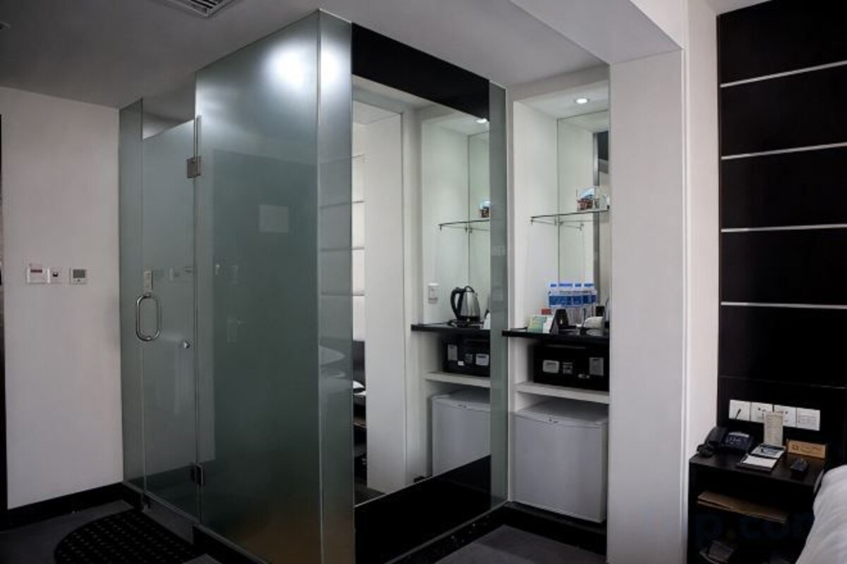 A modern bathroom with a glass shower enclosure, a mirror, and a black shelf with toiletries.