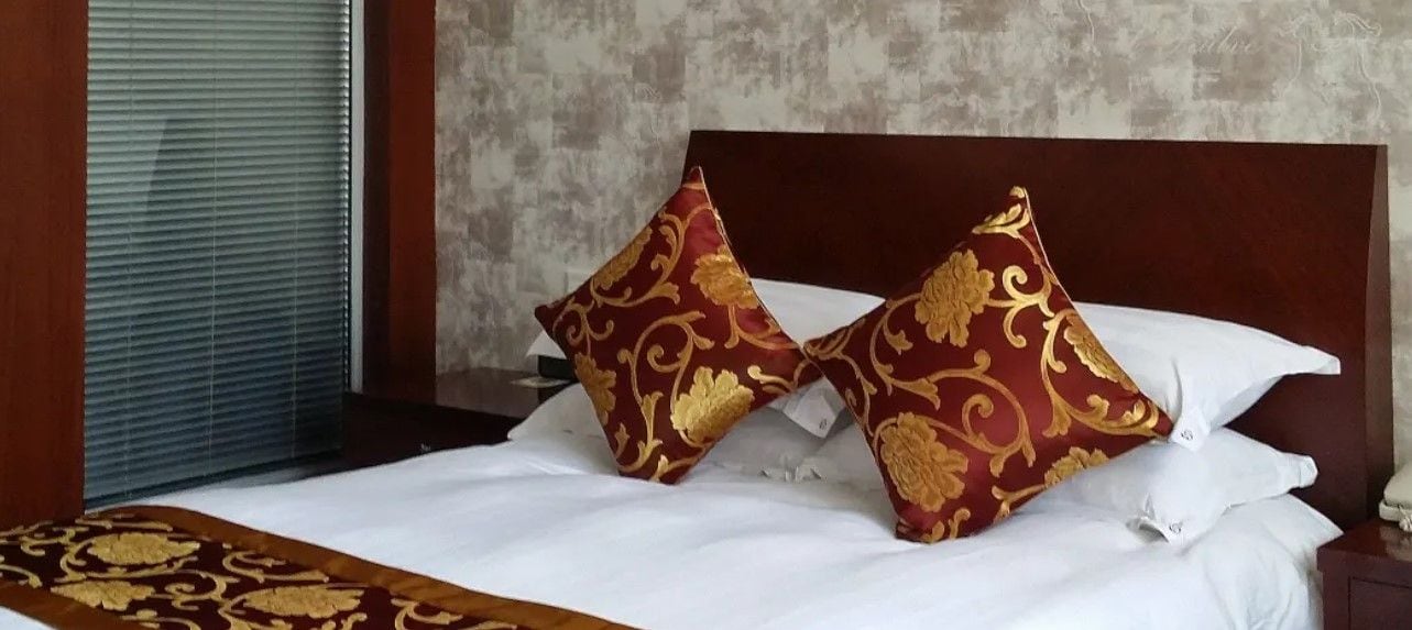 A bed with white linens and two decorative pillows with a gold pattern.