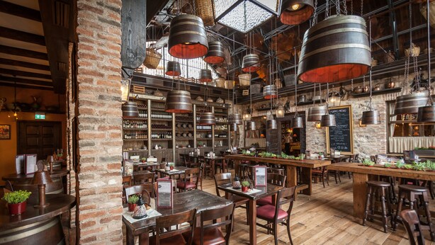 Un restaurante con paredes de ladrillo, mesas de madera y candelabros metálicos colgantes.