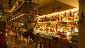 Un bar con estantes llenos de botellas de licor y vasos, una caja registradora y una barra.