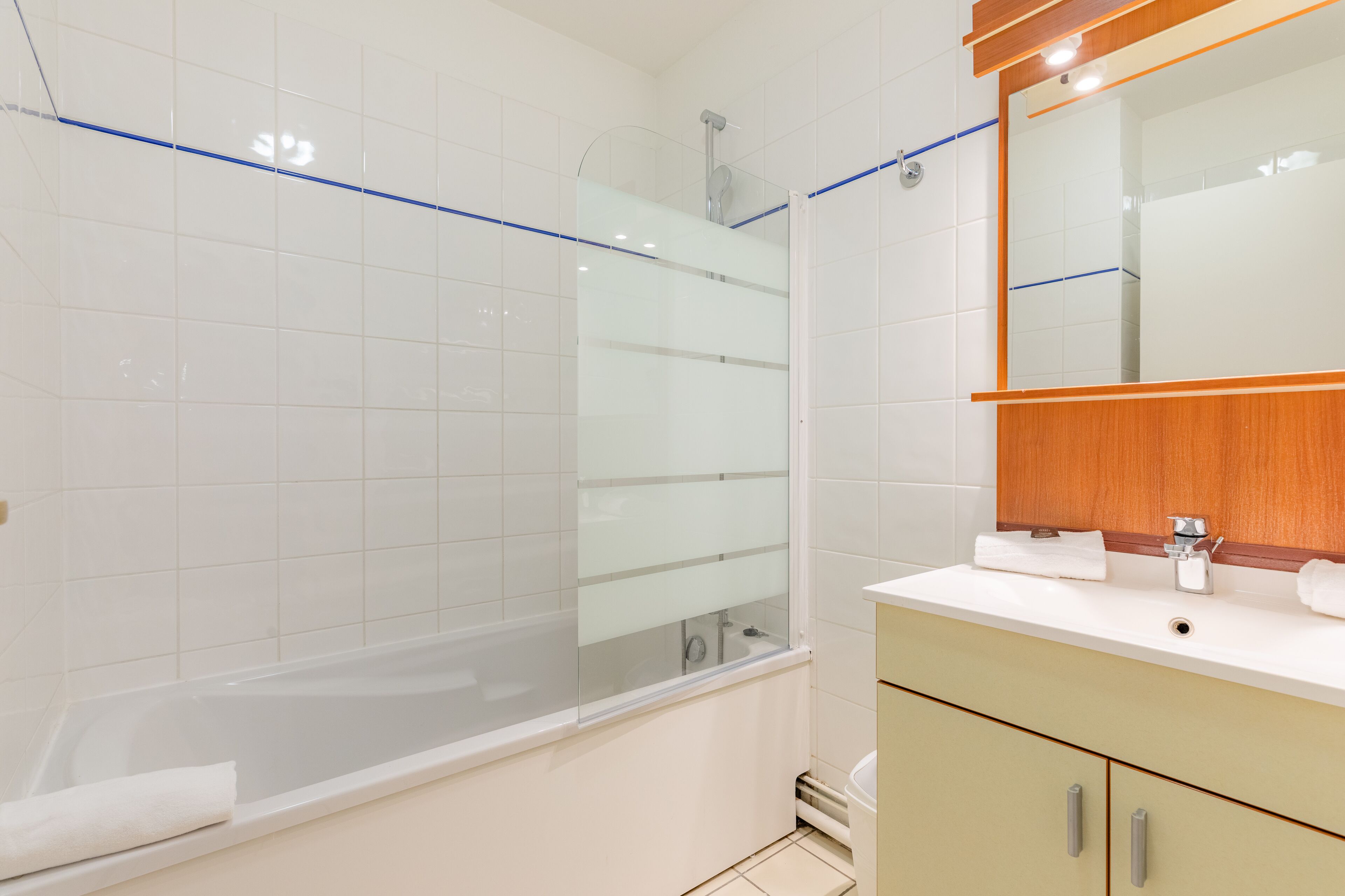A modern bathroom with a glass-enclosed shower, a white sink, and a wooden vanity.