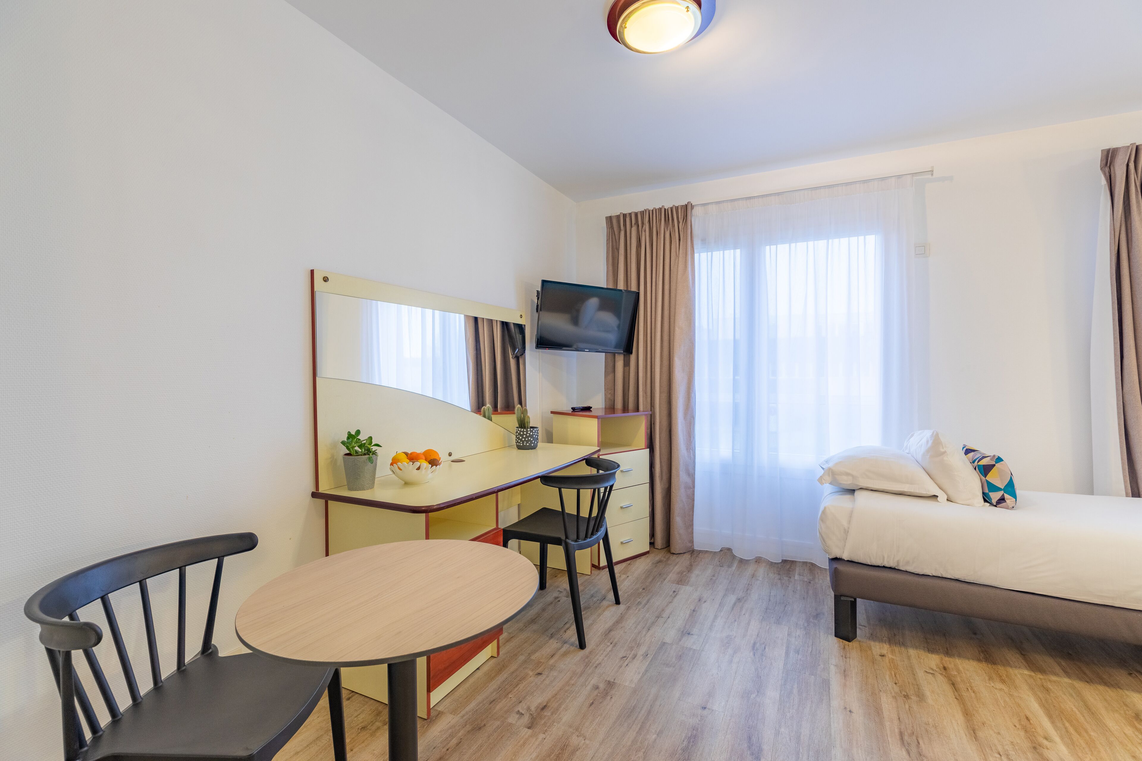 Una habitación de hotel con una cama, un escritorio con silla, un televisor y una ventana con cortinas.