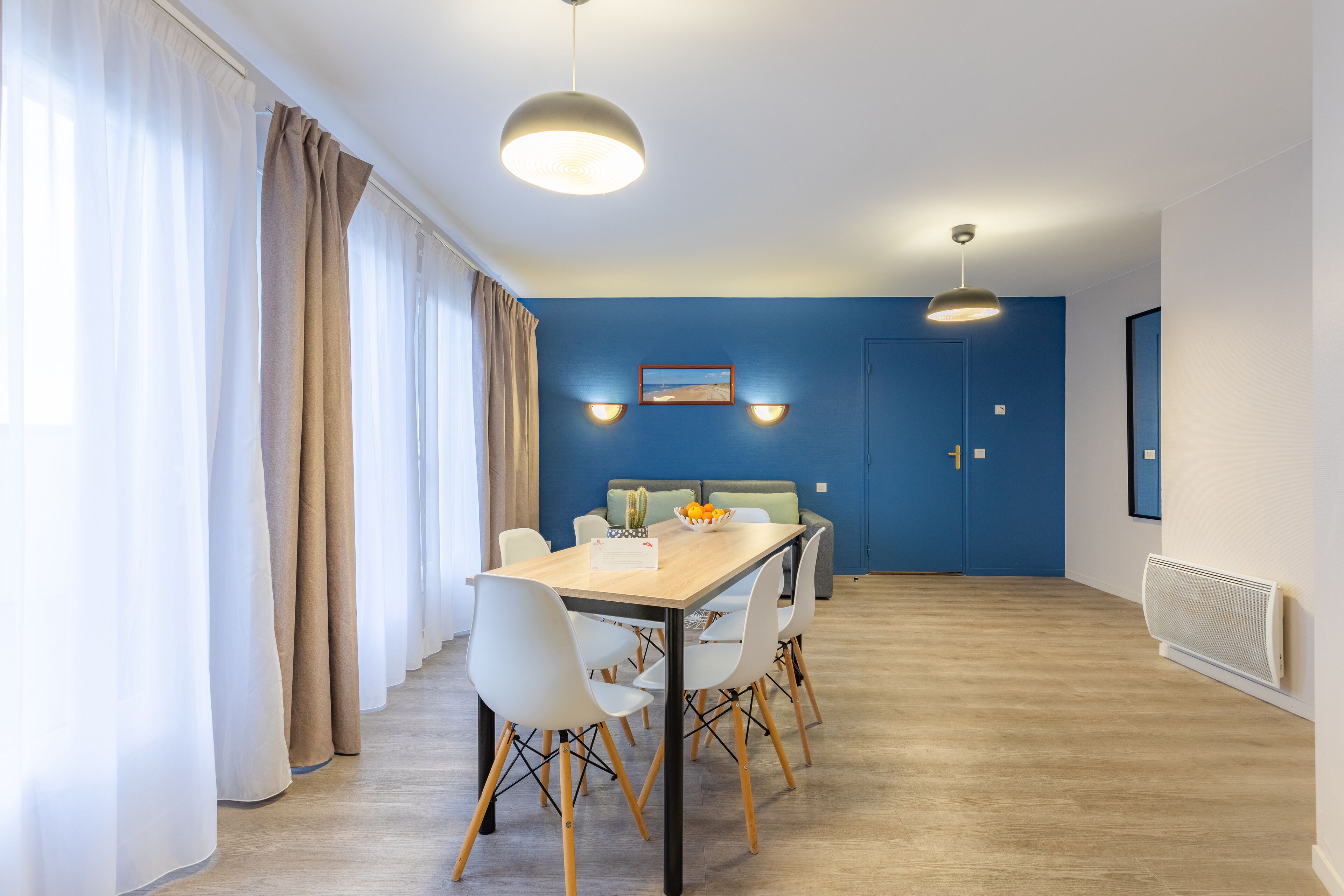 Een eethoek met een houten tafel, witte stoelen en een blauwe accentmuur.